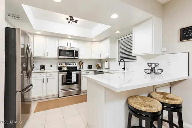 a kitchen with stainless steel appliances granite countertop a sink a stove a refrigerator cabinets and a dining table with chairs