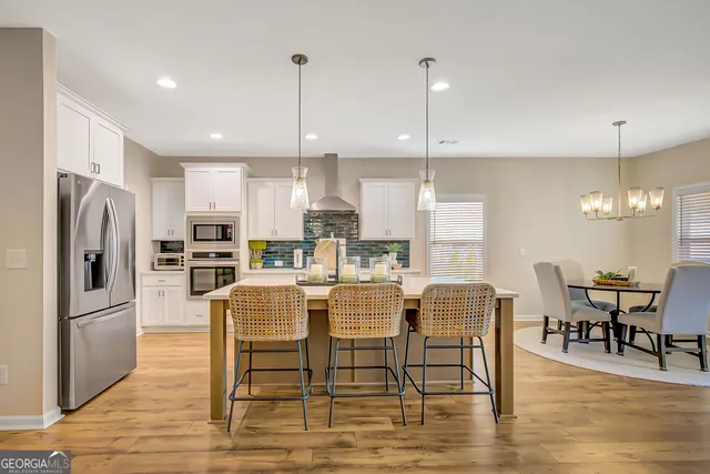 a kitchen with stainless steel appliances kitchen island granite countertop a stove a refrigerator and a dining table with wooden floor