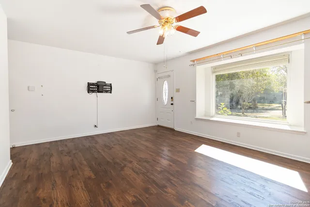 a view of an empty room with a window and wooden floor
