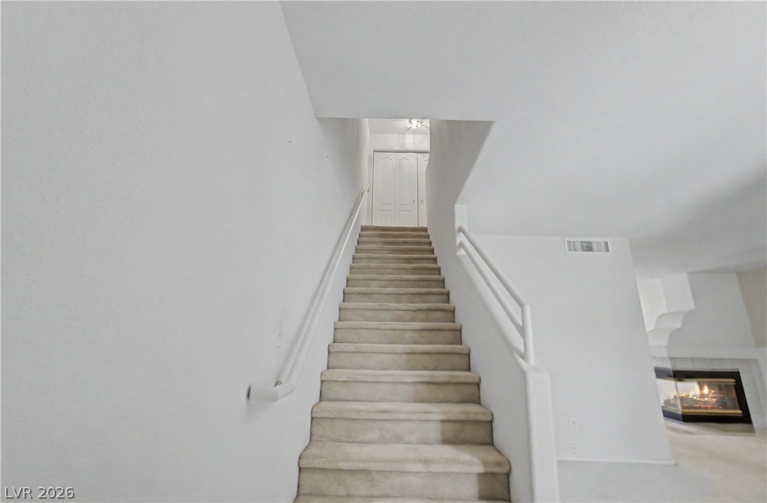 2243 Rugged Mesa Drive Laughlin, NV 89029 - Photo 11 of 32 A carpeted staircase ascends to an upper level, offering a cozy ambiance with a glimpse of a modern fireplace.