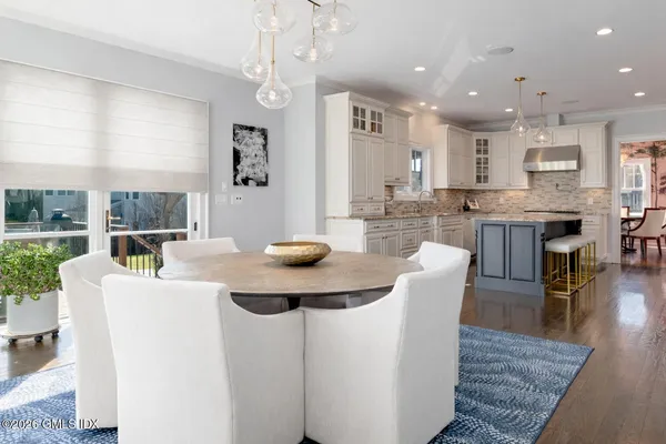 a large white dining hall with stainless steel appliances kitchen island granite countertop a dining table chairs and a large window