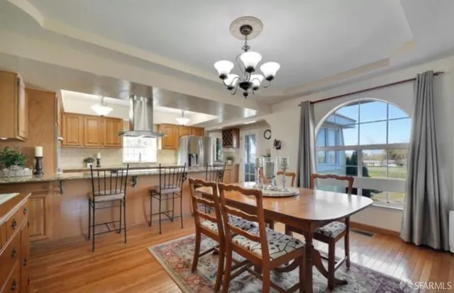 a dining room with stainless steel appliances kitchen island granite countertop a table chairs and a chandelier