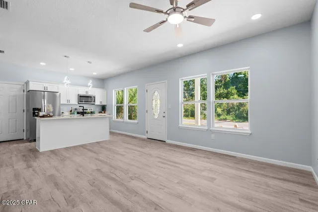 a view of an empty room with kitchen and window