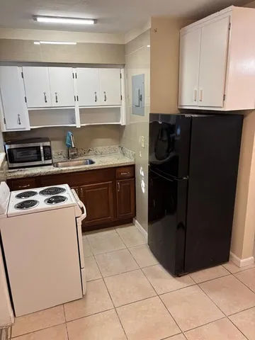 a white kitchen with granite countertop a stove a refrigerator and cabinets