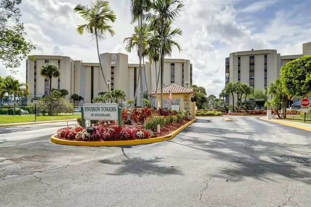 a view of a sign board with flower plants and wooden fence