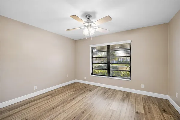 an empty room with wooden floor chandelier fan and windows
