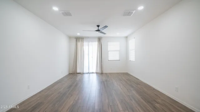 an empty room with wooden floor chandelier fan and windows