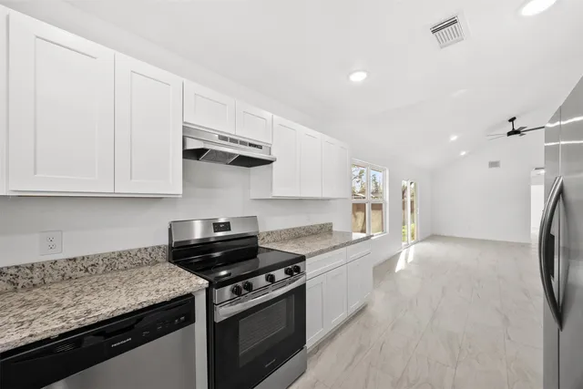 a kitchen with stainless steel appliances granite countertop a stove a refrigerator and a white cabinets