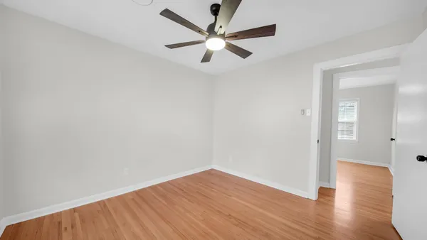 an empty room with wooden floor ceiling fan and windows
