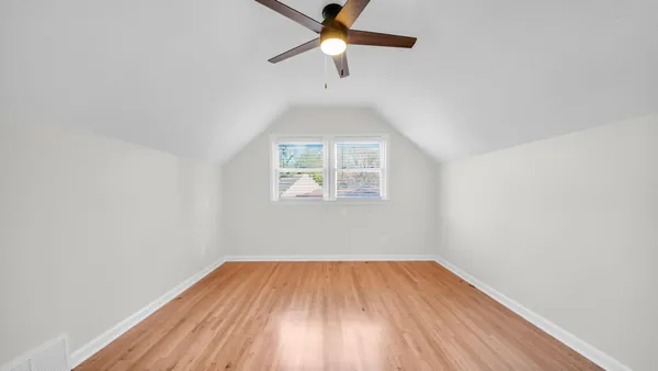 an empty room with wooden floor ceiling fan and windows