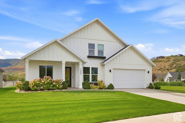 Modern farmhouse exterior with white vertical and horizontal siding, covered entry, attached garage, and mountain scenery