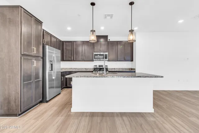 a kitchen with kitchen island a counter top space a sink a refrigerator and wooden floor