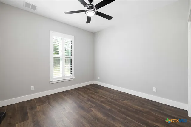 an empty room with wooden floor fan and windows