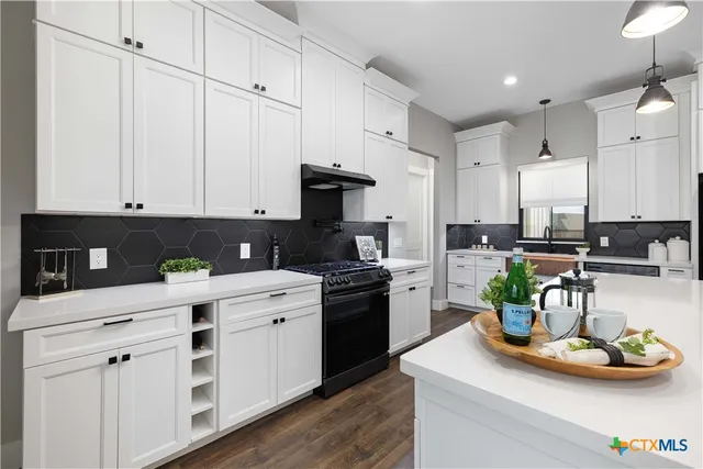 a kitchen with stainless steel appliances granite countertop a sink a stove and white cabinets
