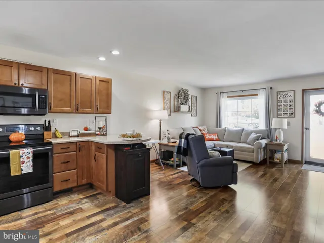 a living room with stainless steel appliances granite countertop wooden floors a stove top oven a granite counter space and a window