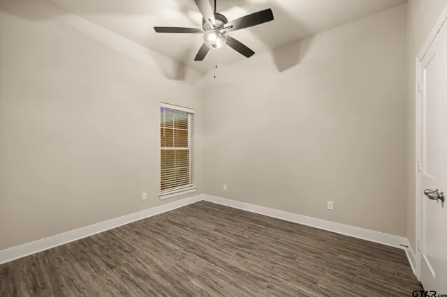 an empty room with wooden floor ceiling fan and windows