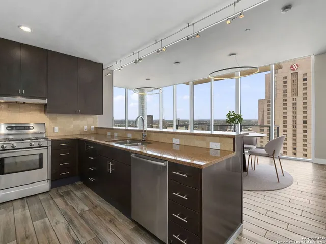 a kitchen with stainless steel appliances granite countertop a stove top oven a sink dishwasher a dining table and chairs with wooden floor