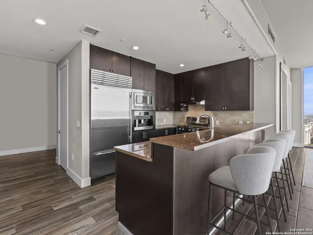 a kitchen with stainless steel appliances granite countertop a refrigerator a stove and a sink with wooden floor