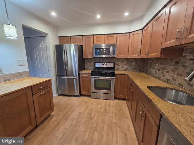 a kitchen with kitchen island granite countertop wooden cabinets stainless steel appliances and a sink