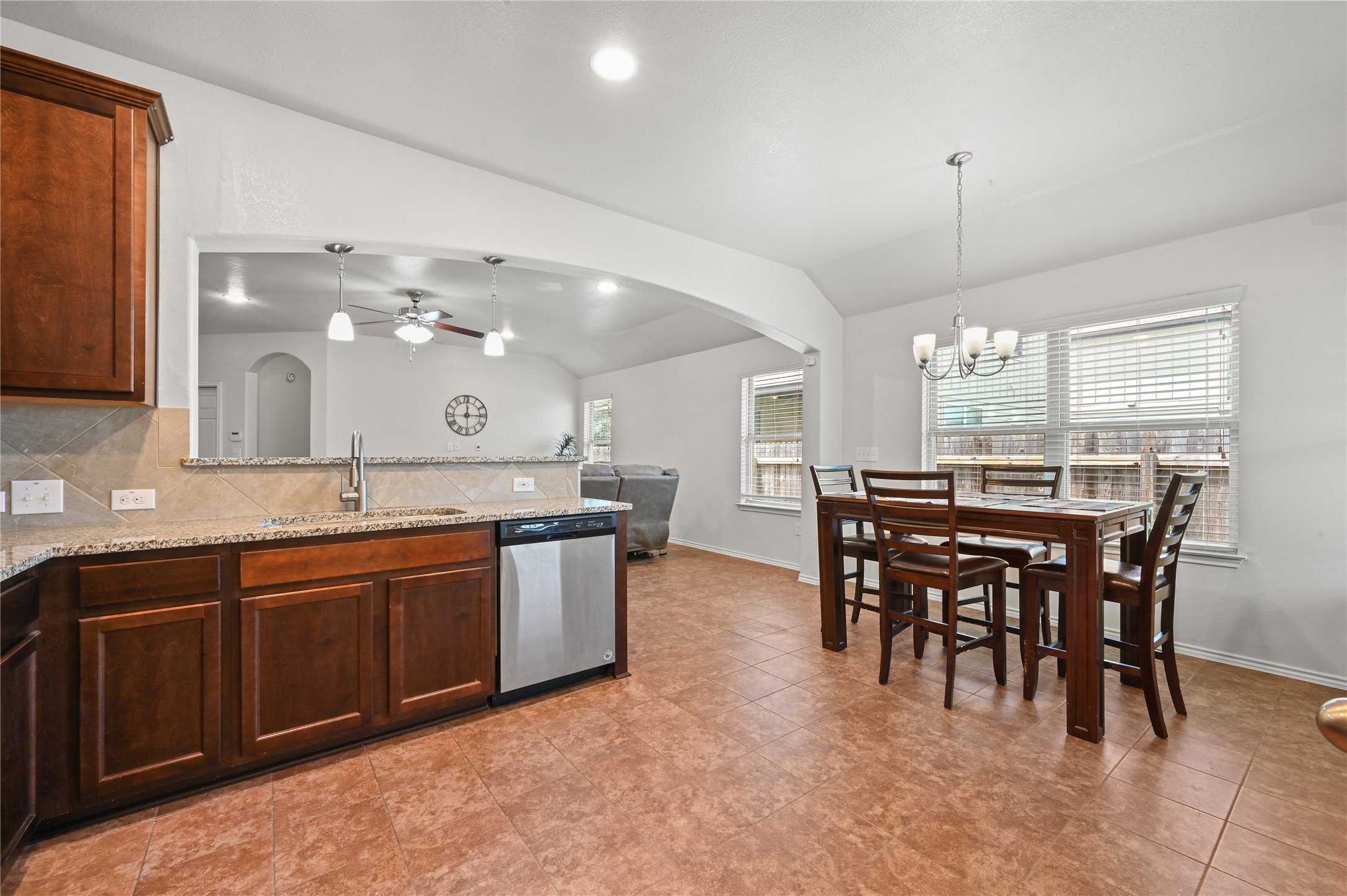 303 Limerick Road Buda, TX 78610 - Photo 9 of 23 Kitchen and dining area featuring warm-toned tile flooring, dark wood-finish cabinetry, light granite countertops, and a stainless steel dishwasher