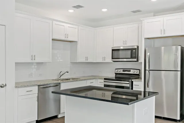 a kitchen with stainless steel appliances granite countertop a sink a stove a refrigerator a microwave and white cabinets