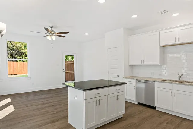 a kitchen with a sink dishwasher and white cabinets with wooden floor