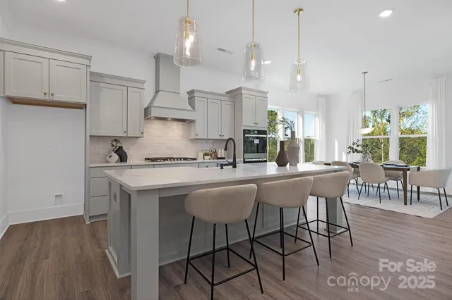 a kitchen with stainless steel appliances granite countertop a stove a sink a refrigerator a dining table and chairs with wooden floor