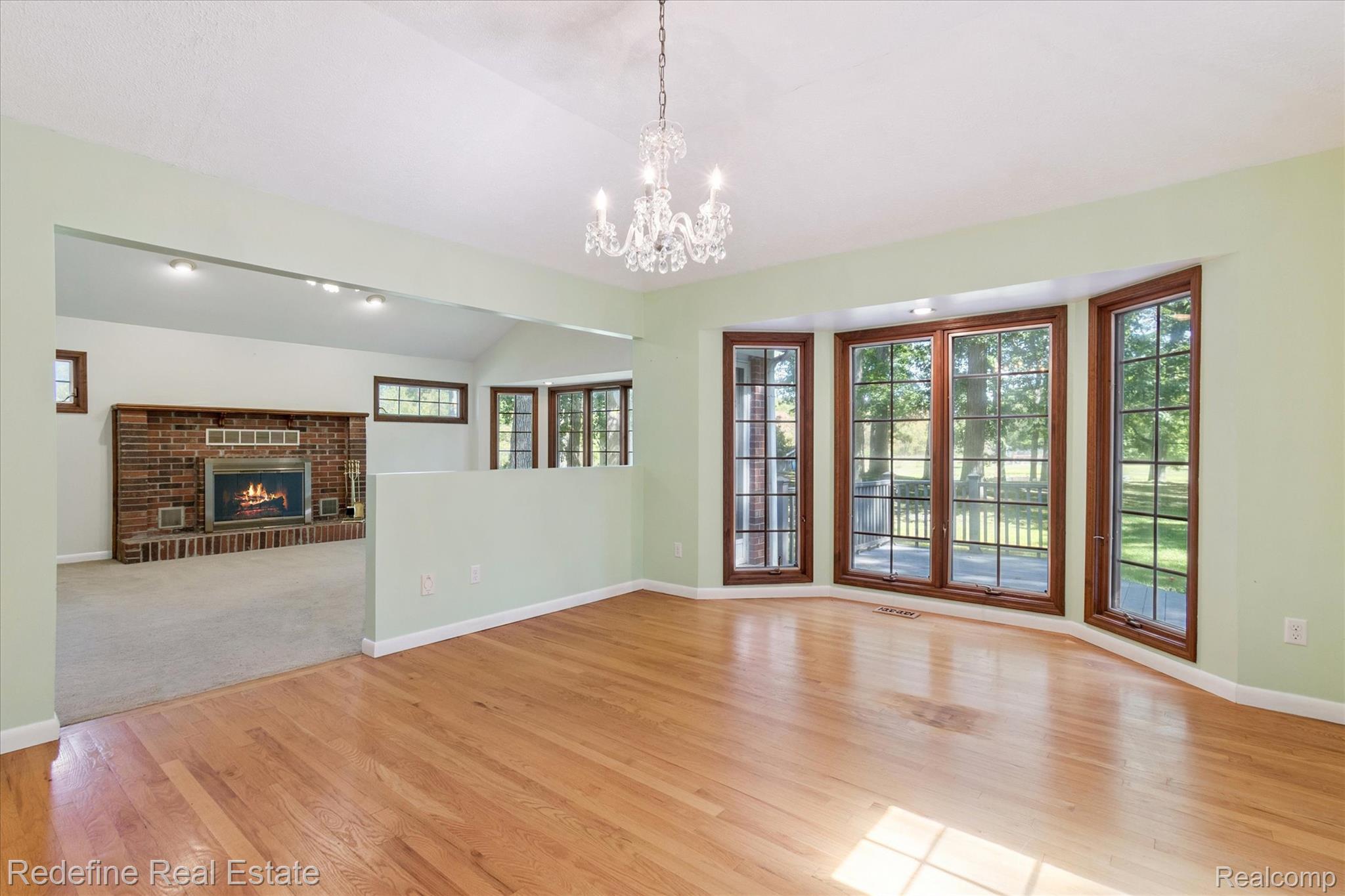 3777 Dorr Road Brighton, MI 48116 - Photo 24 of 77 Unfurnished living room featuring vaulted ceiling, light wood-type flooring, a fireplace, and a chandelier