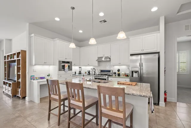 a kitchen with stainless steel appliances kitchen island granite countertop a dining table chairs refrigerator and microwave