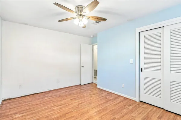 an empty room with wooden floor fan and windows