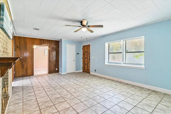 a view of an empty room with window and chandelier fan