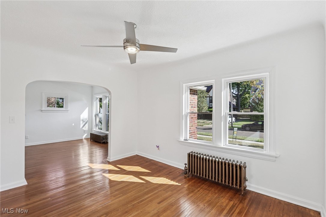 3621 Cedarbrook Road Cleveland, OH 44118 - Photo 13 of 40 Empty room featuring radiator heating unit, hardwood / wood-style flooring, arched walkways, and a ceiling fan