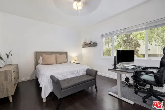 a bedroom with a bed and a computer on the desk next to a large window