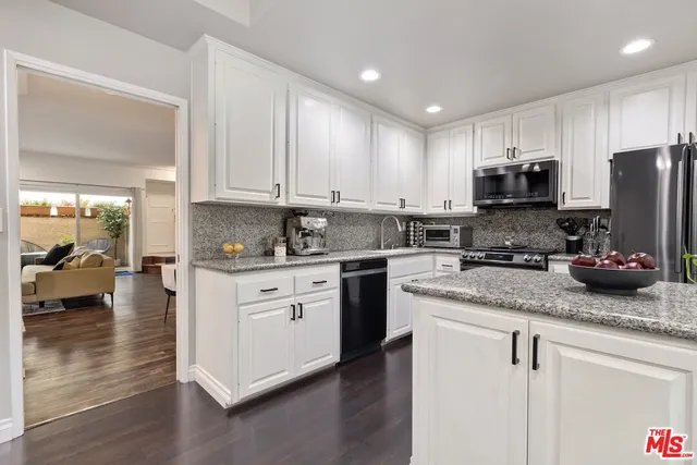 a kitchen with stainless steel appliances granite countertop a stove a sink a refrigerator and white cabinets