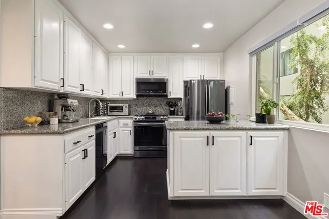 a kitchen with granite countertop white cabinets white appliances a sink and a window