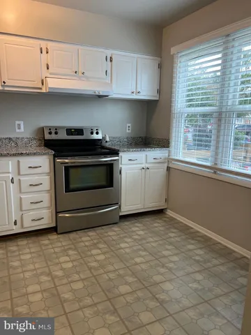 a kitchen with granite countertop a stove a sink and white cabinets