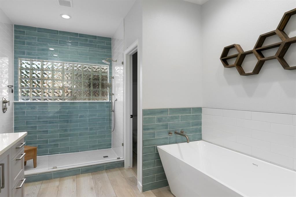 14140 Regency Place Dallas, TX 75254 - Photo 24 of 38 Modern bathroom featuring a freestanding soaking tub with wall-mounted faucet, a walk-in shower with glass enclosure, teal subway tile accents, glass block shower window, and wood-finish flooring