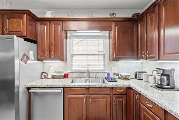 a kitchen with stainless steel appliances granite countertop a refrigerator a stove and a sink with wooden cabinets