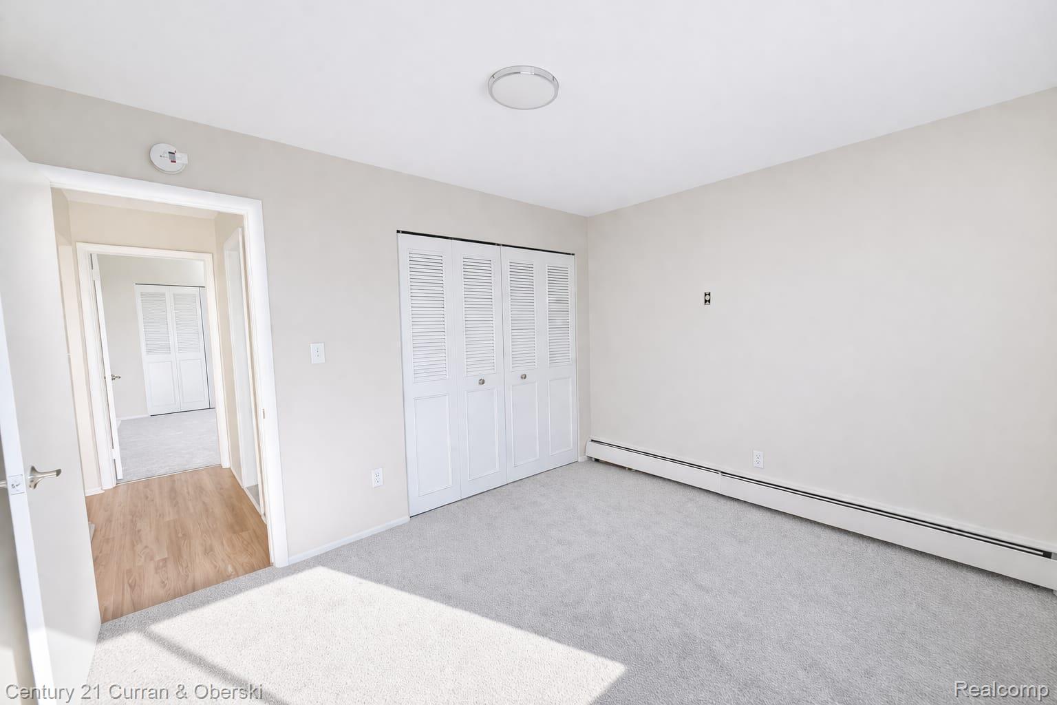 6015 Southfield Road, Unit 6 Detroit, MI 48228 - Photo 8 of 10 Unfurnished bedroom featuring light carpet, a baseboard radiator, and a closet