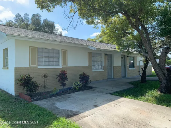 front view of a house with potted plants and a large tree