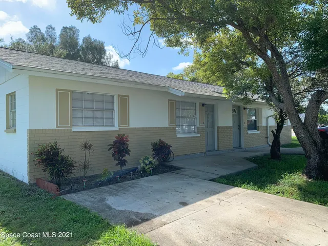 front view of a house with potted plants and a large tree
