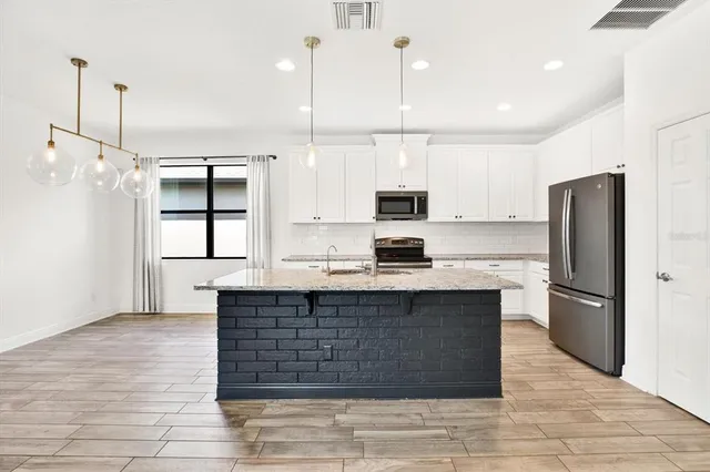a kitchen with stainless steel appliances granite countertop a refrigerator a sink dishwasher a oven and a view of living room with wooden floor