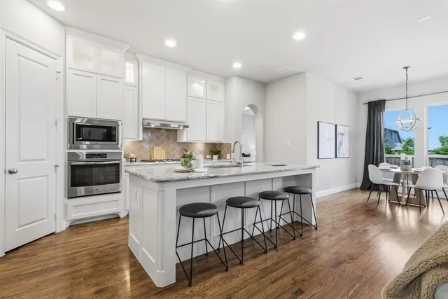 a kitchen with stainless steel appliances a microwave a stove a sink dishwasher a refrigerator and white cabinets with wooden floor