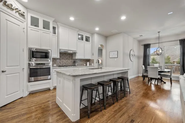 a kitchen with stainless steel appliances granite countertop a stove top oven a sink dishwasher a dining table and chairs with wooden floor