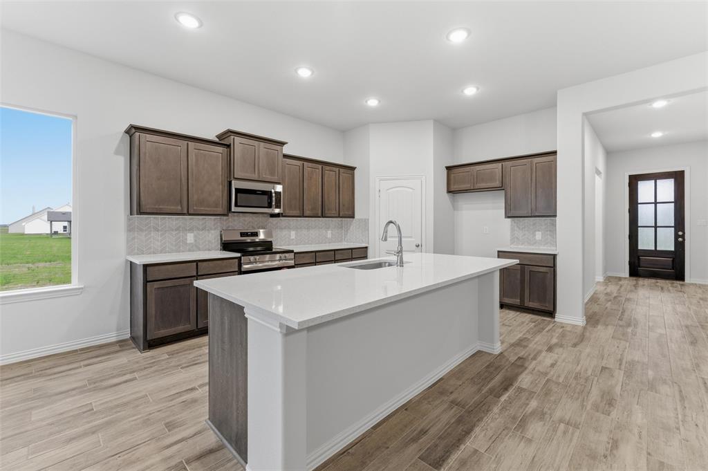 119 Hillview Trail Decatur, TX 76234 - Photo 21 of 30 Modern kitchen featuring wood-finish flooring, recessed lighting, an island with an integrated sink, dark wood cabinetry, and stainless steel appliances