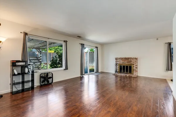 a view of an empty room with wooden floor fireplace and a window