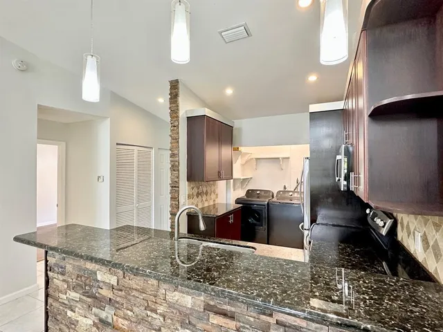 a kitchen with stainless steel appliances kitchen island granite countertop a refrigerator a stove and a sink with wooden floor