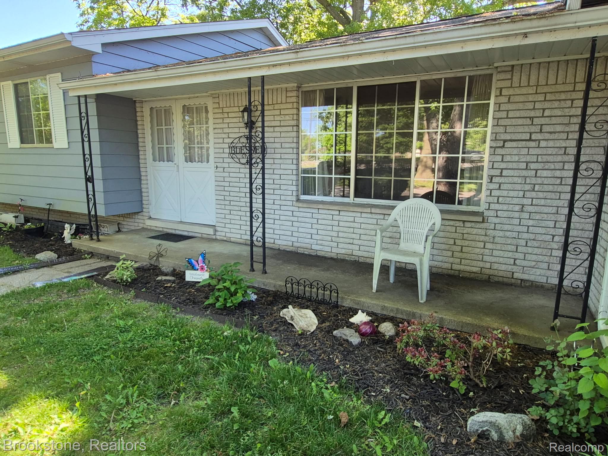 4295 Sashabaw Road Waterford, MI 48329 - Photo 3 of 37 Exterior featuring white brick facade, light blue siding, a covered porch with decorative black metal columns, and a landscaped garden bed