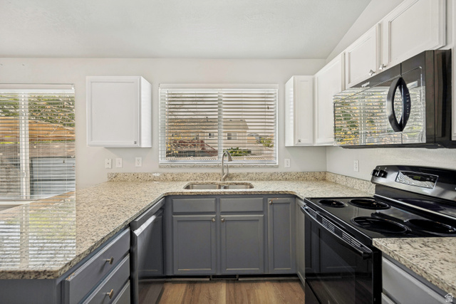 5529 Ridge Hollow Way Kearns, UT 84118 - Photo 7 of 23 U-shaped kitchen featuring wood-finish flooring, two-tone cabinetry, light-toned countertops, and a black appliance suite with a built-in microwave