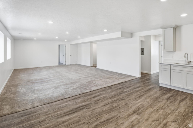 3636 West 910 South Syracuse, UT 84075 - Photo 49 of 70 Spacious room featuring wood-finish flooring transitioning to neutral-toned carpeting, recessed lighting, and a kitchenette area with light gray cabinetry, a countertop, and a stainless steel sink with a gooseneck faucet